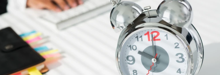  Un reloj despertador metálico se encuentra en una mesa junto a un bloc de notas con separadores de colores. 