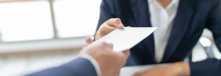  Dos personas en trajes formales intercambian un sobre blanco. 