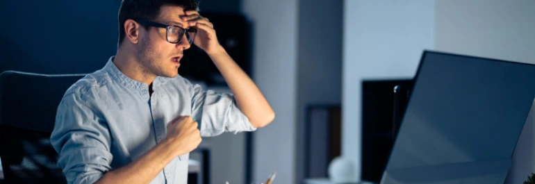  Un hombre con gafas frente a una computadora parece sorprendido o preocupado mientras se toca la cabeza. 