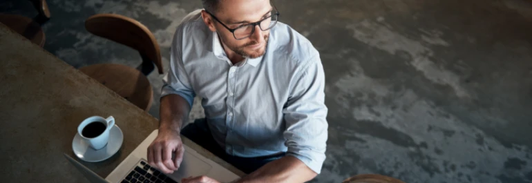 Un hombre con gafas usa una computadora portátil mientras toma café. 