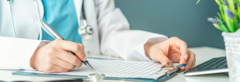  Una persona con bata blanca llena un formulario sobre una mesa. 