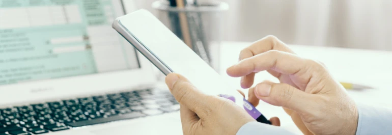  Una persona utiliza un smartphone frente a una computadora portátil. 