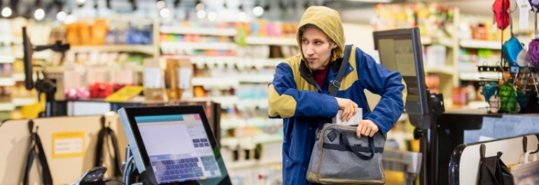  Una persona con capucha, sin vigilancia, colocando algo en su bolso dentro de una tienda. 