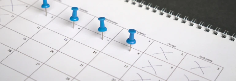  Un calendario con tachones en algunos días y chinchetas azules marcando otros. 