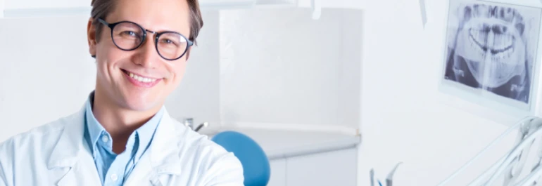  Un dentista sonriente en su consultorio junto a una radiografía dental. 