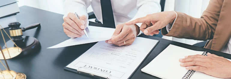  Dos personas revisan un contrato en una oficina con símbolos legales. 