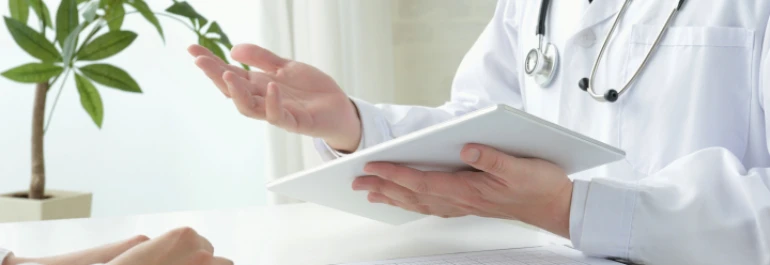  Un médico con bata blanca sostiene una tableta mientras habla con un paciente. 