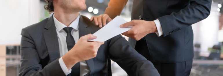  Dos personas en trajes formales intercambian un sobre en una oficina. 
