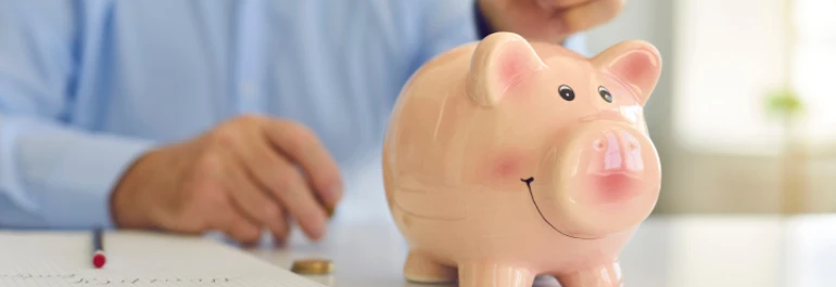  Una persona coloca monedas junto a una alcancía de cerdito sobre un escritorio. 