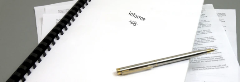  Un informe encuadernado con una pluma sobre él y hojas sueltas alrededor. 