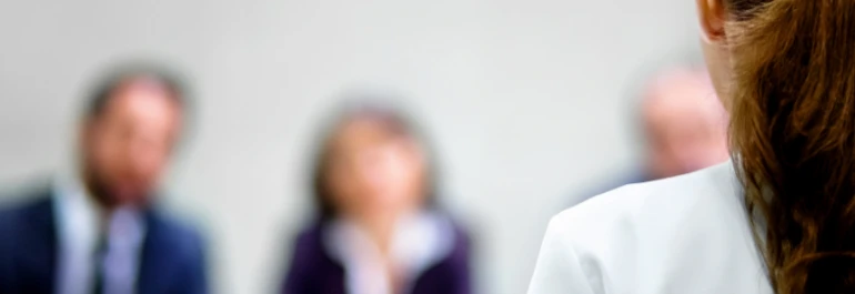  Una persona de espaldas frente a un panel de entrevistadores borrosos. 