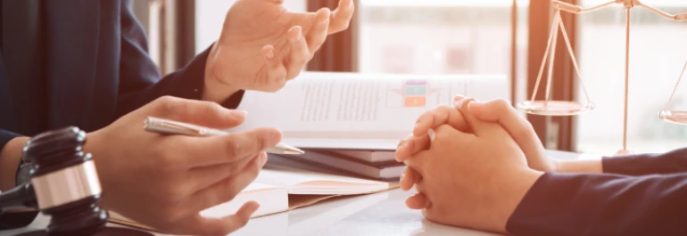  Dos personas conversan en una mesa con un mazo y una balanza simbólica de justicia. 