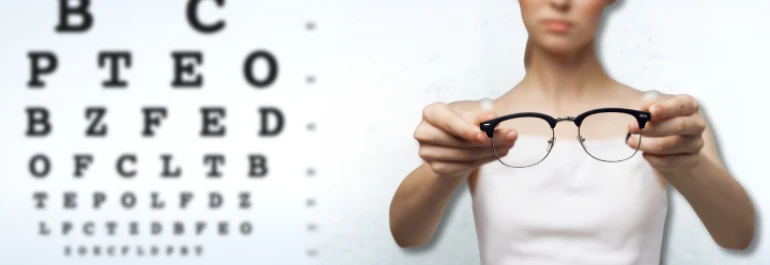  Una persona sosteniendo unas gafas frente a una tabla de examen visual. 