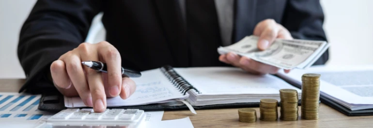  Una persona está usando una calculadora y contando dinero en un escritorio. 