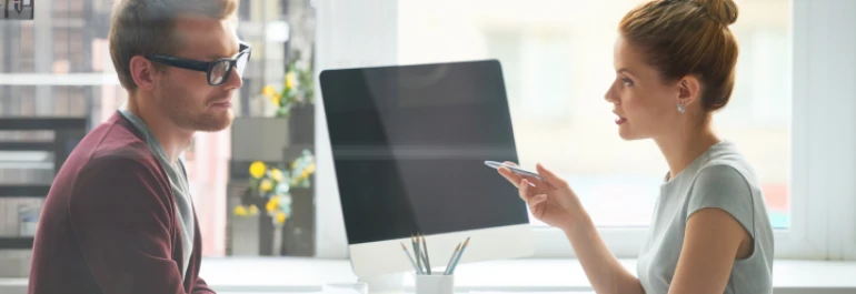  Dos personas conversan en una oficina junto a una computadora. 