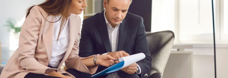  Dos personas revisan documentos sentadas en una oficina. 