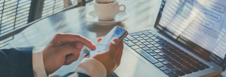  Una persona usando un teléfono móvil frente a una laptop con una pantalla de inicio de sesión. 