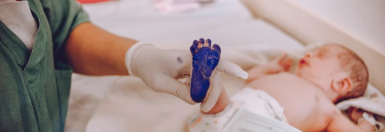  Bebe en el hospital, con pintura azul en su pie que es sostenido por un médico 
