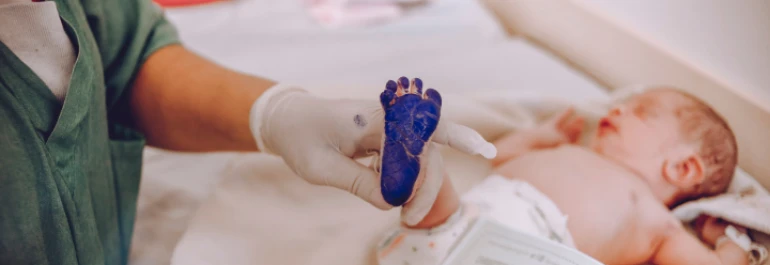  Bebe en el hospital, con pintura azul en su pie que es sostenido por un médico 