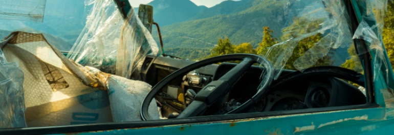  Interior de un vehículo antiguo con parabrisas roto y paisaje montañoso al fondo. 