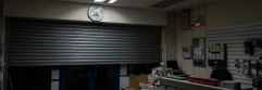  tienda cerrando con la puerta a medio bajar, con un reloj encima y la alarma puesta 
