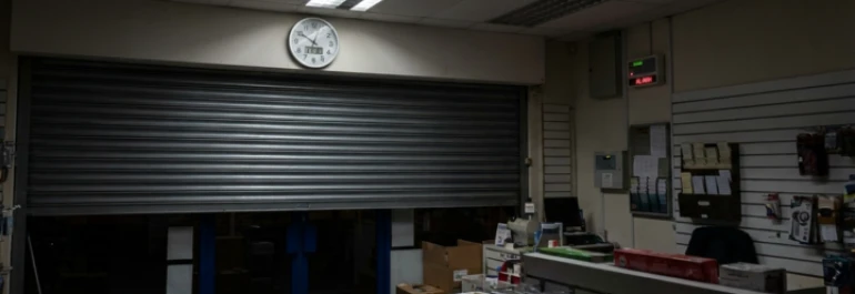  tienda cerrando con la puerta a medio bajar, con un reloj encima y la alarma puesta 