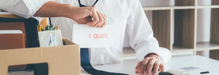  persona con camisa y corbata junto a caja en oficina sujetando cartel que pone I quit 