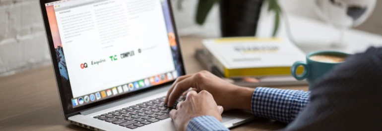  Una persona trabajando en una laptop con una taza de café y libros en el escritorio. 