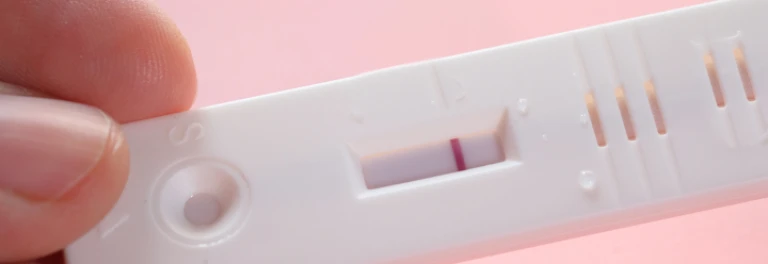  Persona sujetando un test de embarazo con una raya roja 