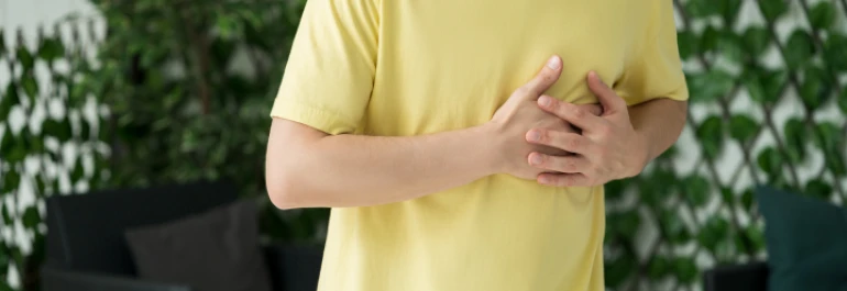  Hombre con camiseta amarilla sujetándose el pecho con ambas manos 
