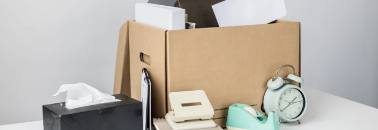  Materiales de oficina empacados en una caja sobre una mesa con un fondo gris 