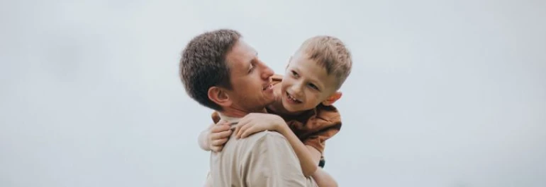  Un hombre carga a un niño en sus brazos mientras ambos sonríen. 