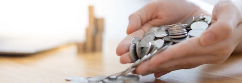  Manos dejando caer monedas plateadas sobre la mesa 