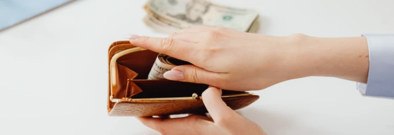  Una persona guarda billetes enrollados en una billetera marrón. 