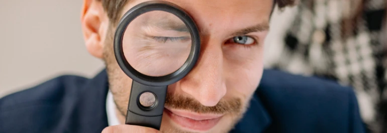  Hombre de ojos claros, barba y con traje viendo a través de una lupa 