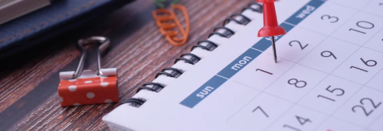  Calendario en cuaderno junto a una pinza naranja con lunares blancos y clip de zanahoria 