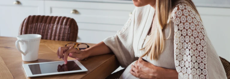  Mujer embarazada trabajando frente a ipad que está en una mesa de madera 