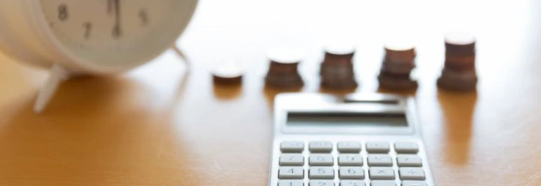  Una calculadora, monedas apiladas y un reloj sobre una mesa. 