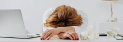  Mujer apoyada sobre sus brazos en un escritorio blanco junto a su laptop y papeles arrugados 