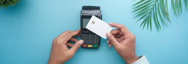  Dos manos pasando tarjeta sobre datafono sobre fondo celeste con plantas 