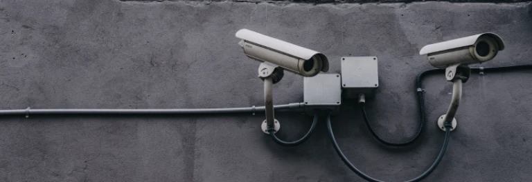  Dos cámaras de seguridad apuntando al mismo sitio sobre una pared gris 