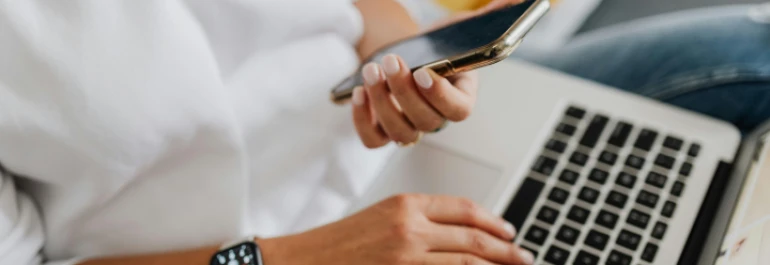  Persona revisando el móvil mientras trabaja en portátil 