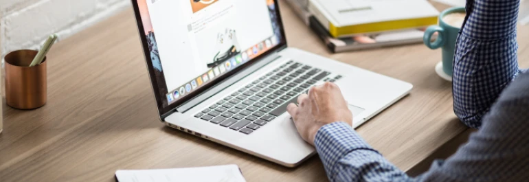  Persona trabajando en una laptop sobre un escritorio con libros y una taza de café. 